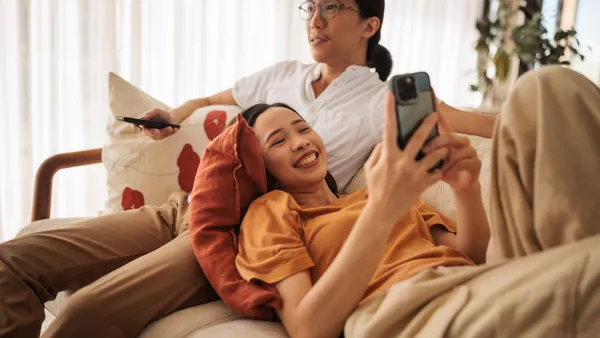 A smiling woman uses her phone while a man watches TV in the living room