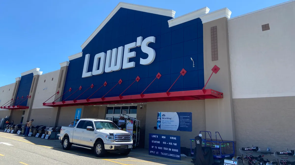 A white truck is parked in front of a Lowe's store on a clear, bright day.