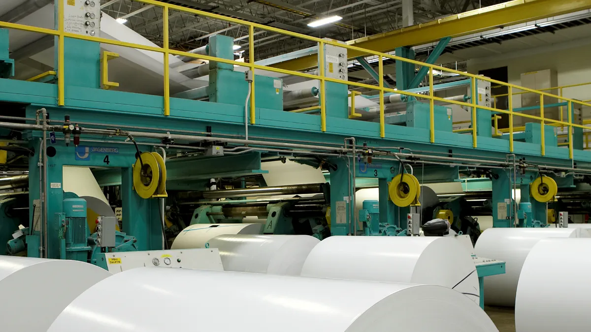 Large rolls of paper are lined up in an industrial facility.