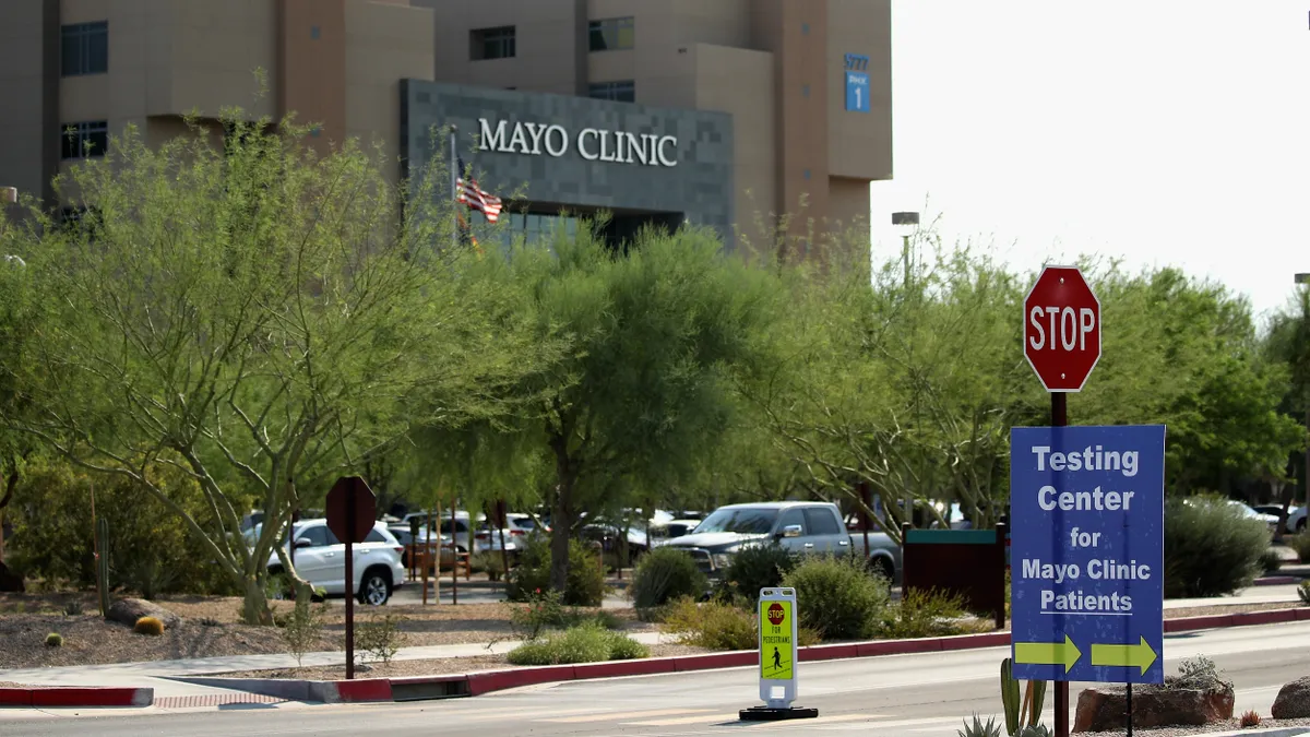 A picture of the mayo clinic with a stop sign in front of the building. A sign is attached to the stop sign signaling coronavirus testing for mayo clinic patients.