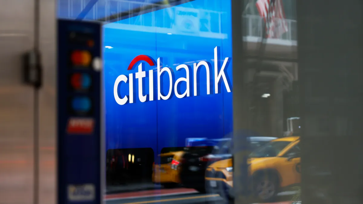 A sign reads "Citibank" in a branch window, which reflects an American flag and taxi cabs on the street.