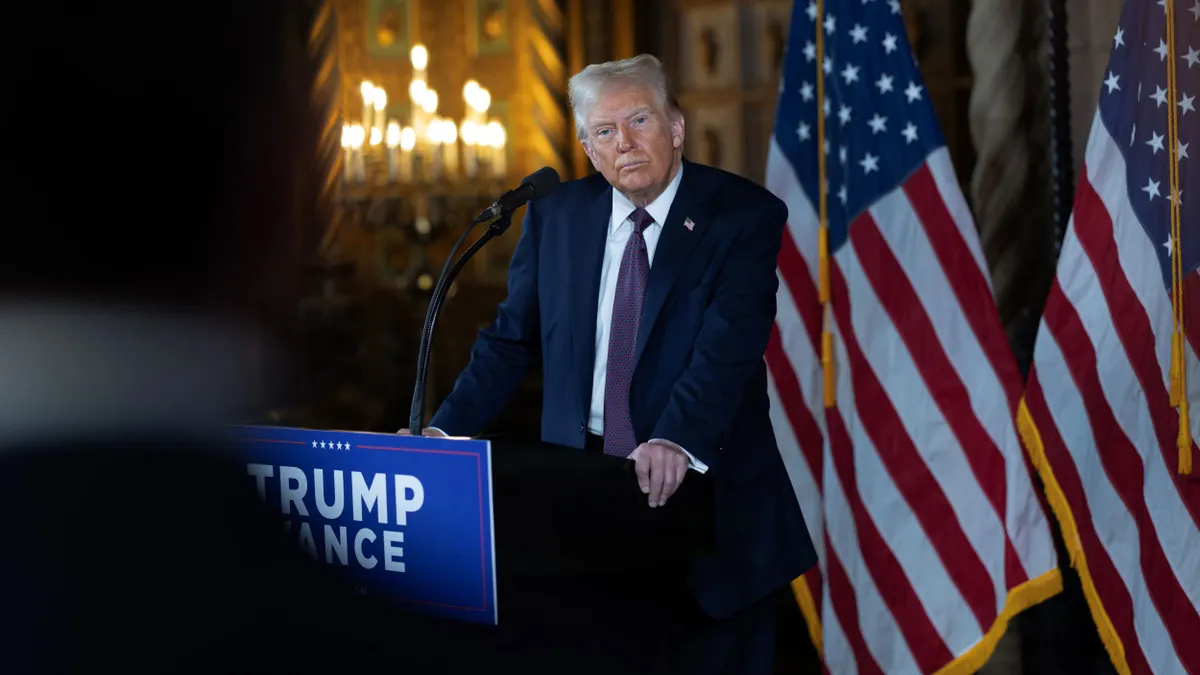 A picture of President-elect Donald Trump standing behind  a podium at a press conference with two American flags in the background.