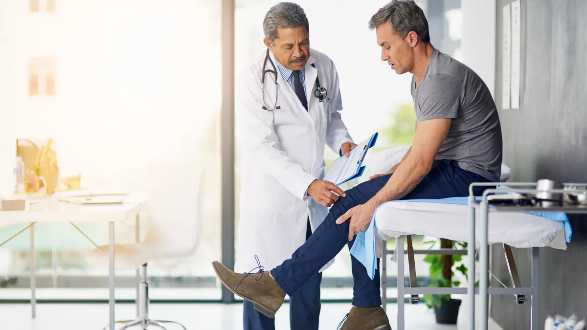 A doctor checks the knee of a patient seated on an examination table.