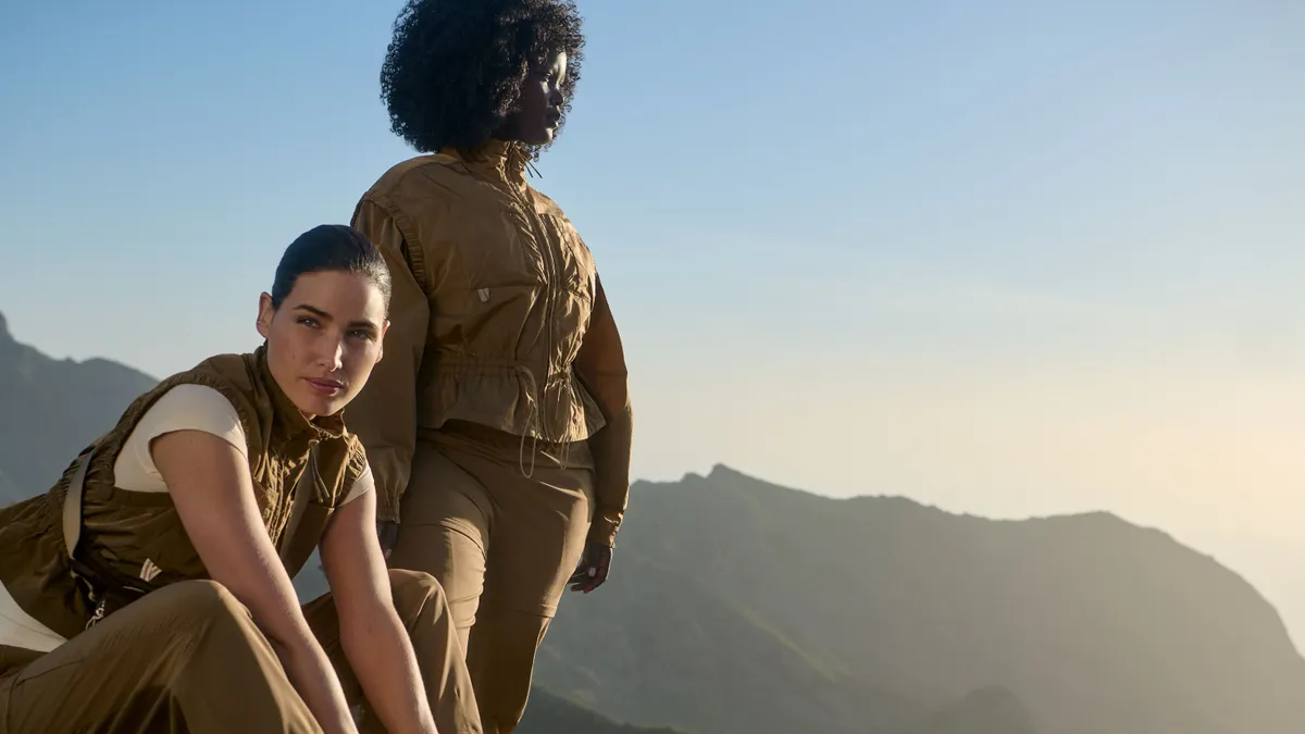 Two people stand on a mountain wearing brown activewear from a Merrell collaboration with Sweaty Betty.