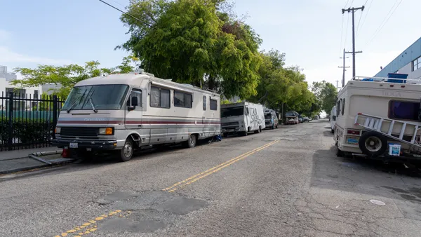 Worn recreational vehicles are parked on the sides of a city street.