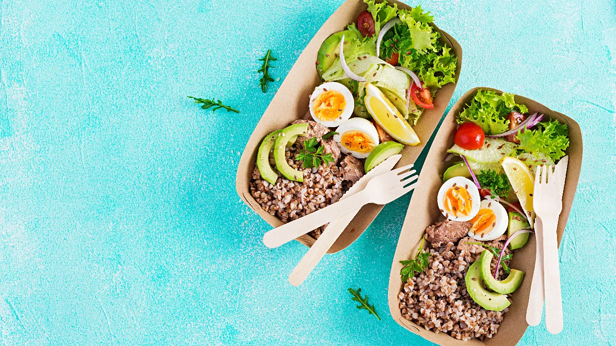 Healthy food delivery. Lunch- Buckwheat porridge, sliced tuna, boiled egg and fresh vegetable salad in zero waste containers on blue background.