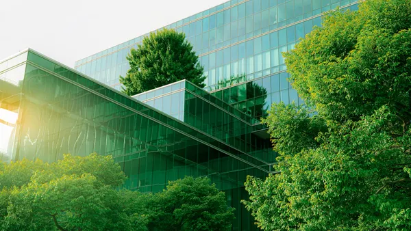 A facade of a sustainable glass office building with a tree for reducing carbon dioxide.