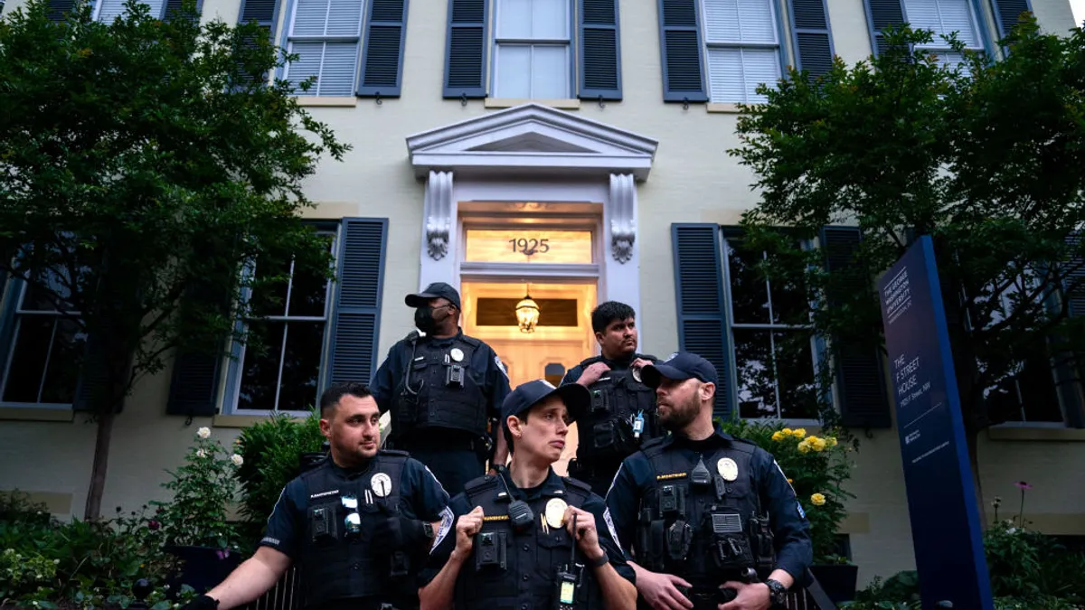 Five people in police uniforms stand on the steps leading up to a historic city home.