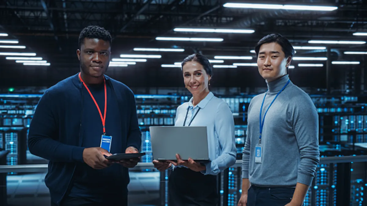 Team of data center system administrators and IT specialists use laptop and tablet computers.