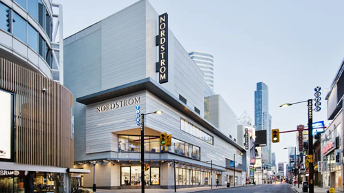 A city street, with a modern, light-gray department store featured on the right.