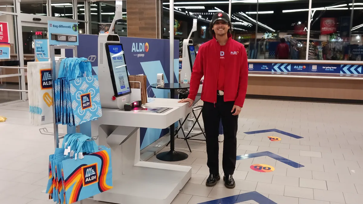 Worker stands next to checkout counter at grocery store.