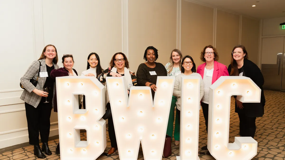 A group of women pose behind a sign reading BWIC.