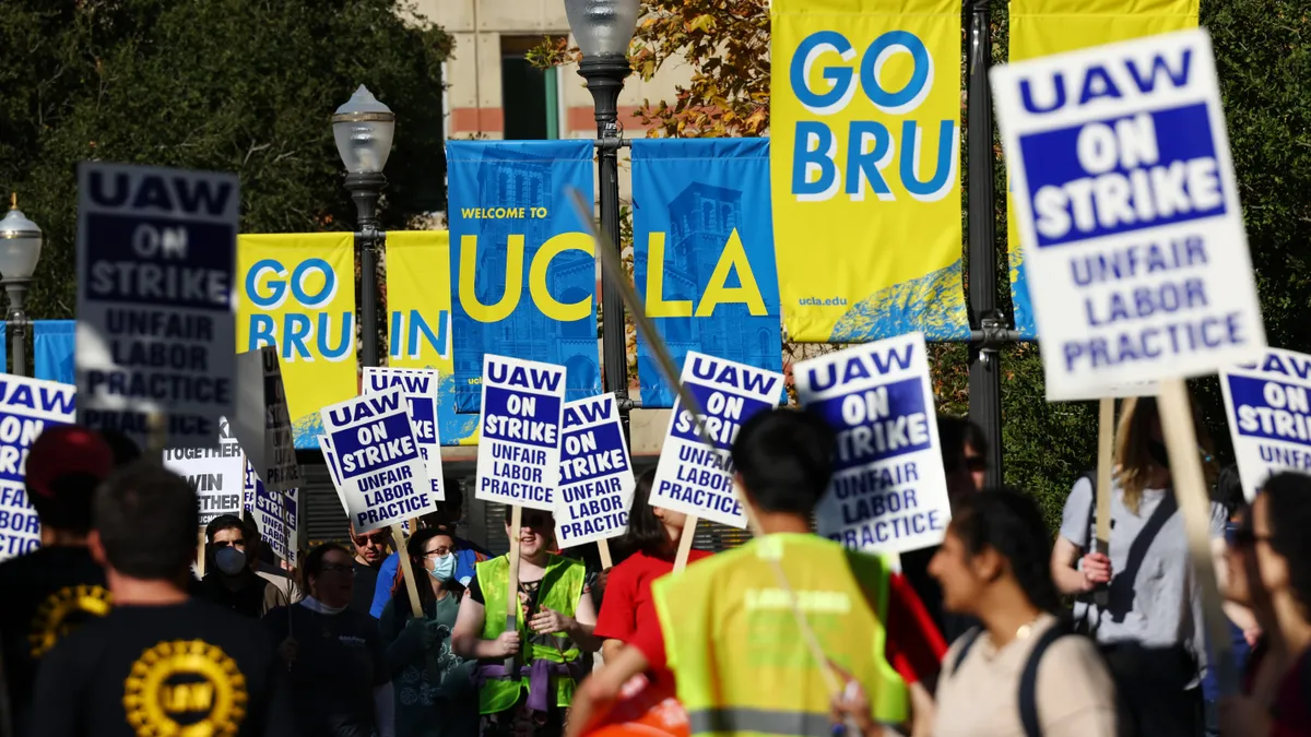 Picket signs can be seen in front of a UCLA sign.