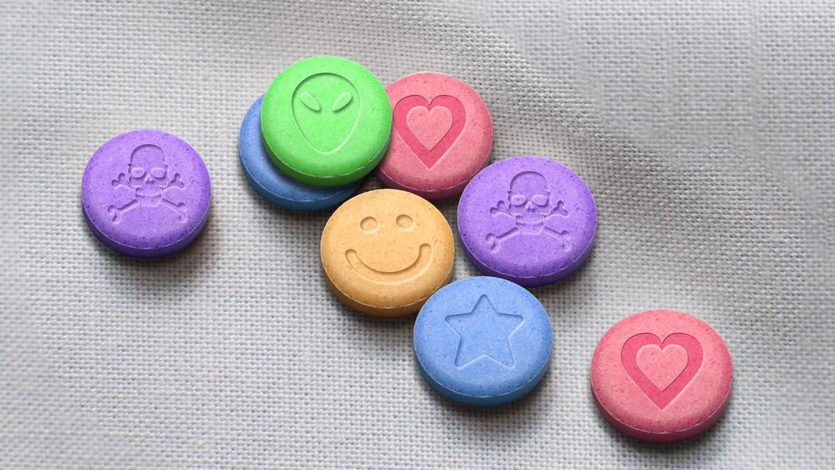 Multicolored MDMA pills are seen on a white fabric background in this photo illustration.