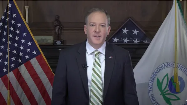 Man standing in a suit in front of a U.S. and EPA flags.