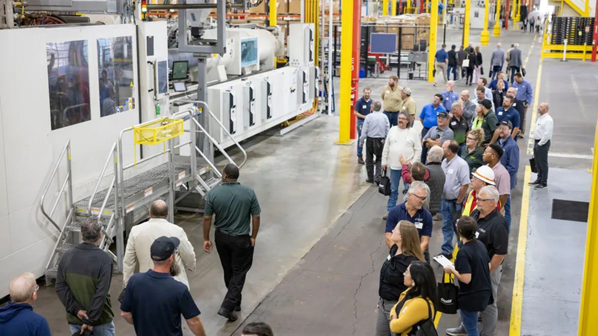 Dozens of people viewing heavy equipment in an industrial facility.
