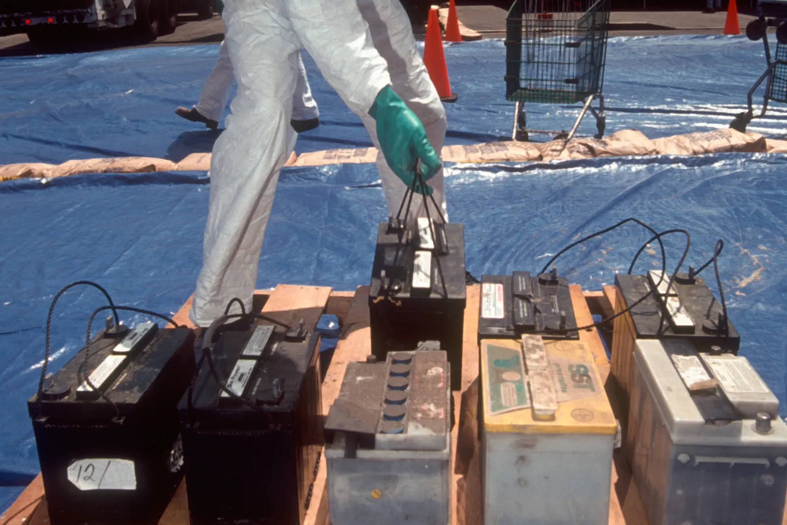 A worker in a protective suit manages used batteries on top of a tarp