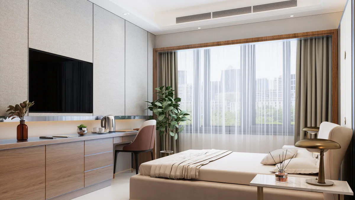 The interior of a hotel room with bed, desk, TV and cityscape from the windo