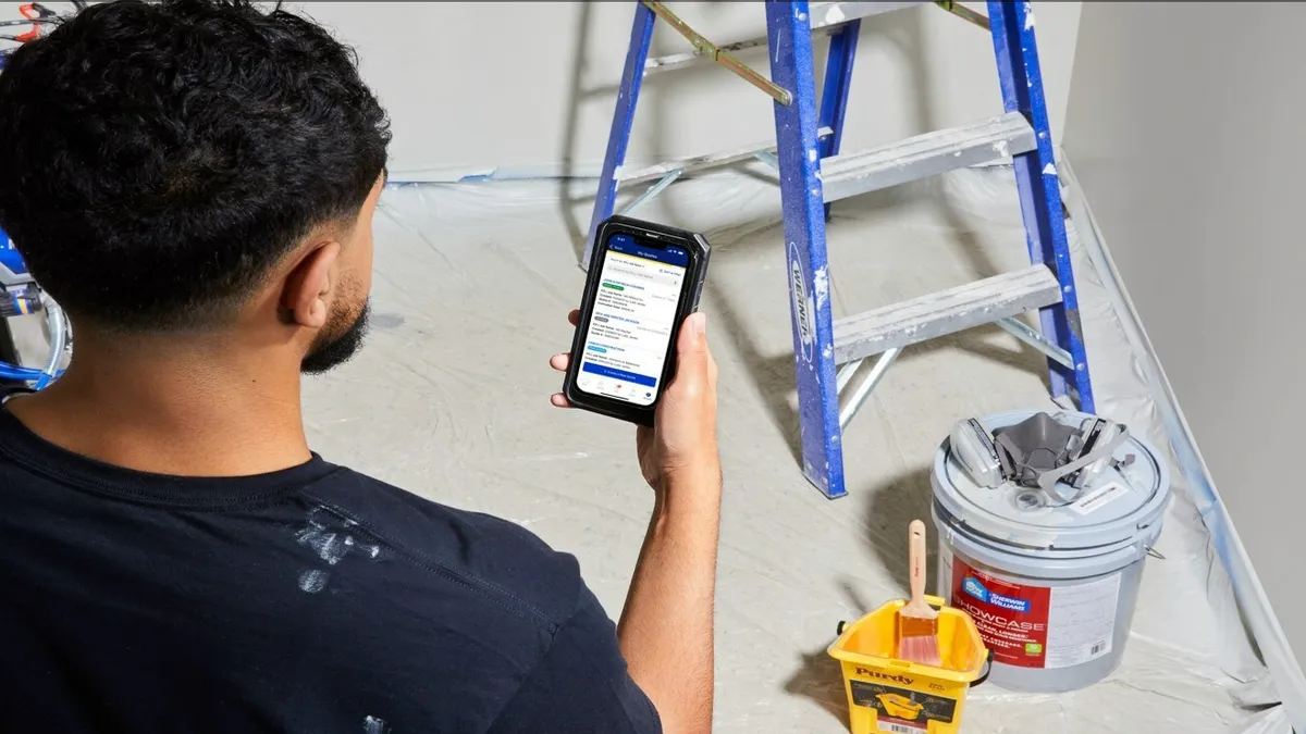 Person holds a mobile phone with Lowe's on the screen next to a ladder.