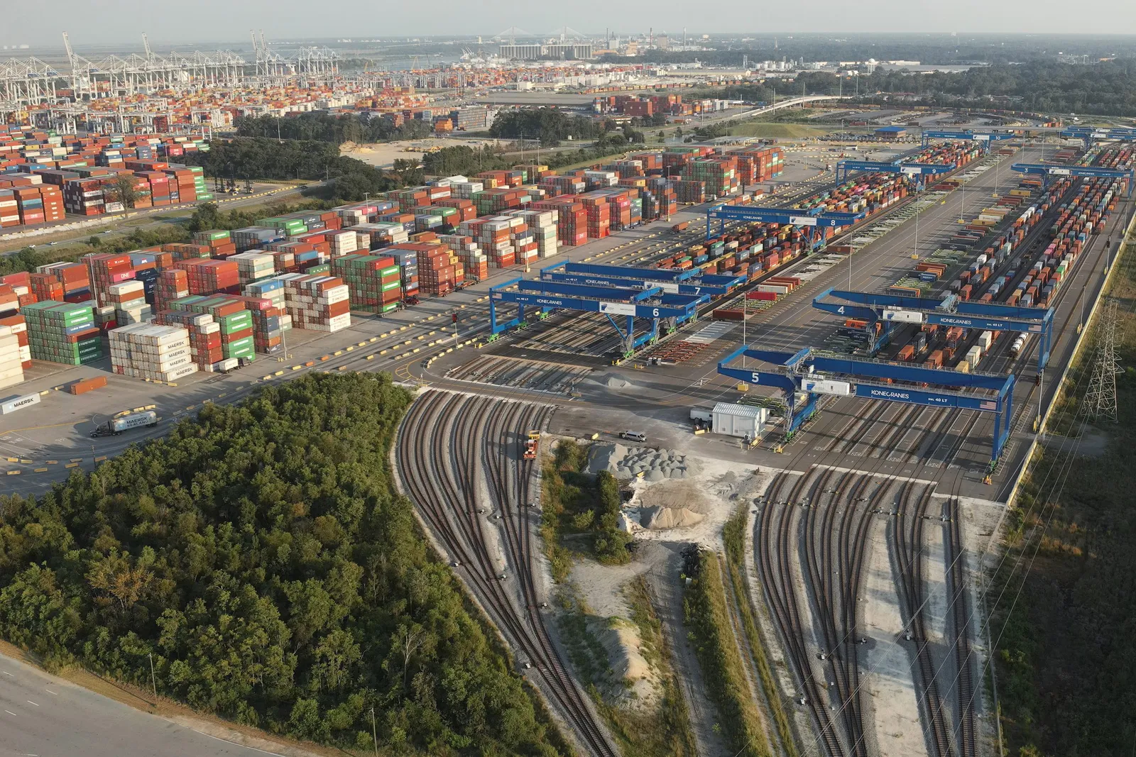 An aerial view of  shipping containers and rail trackers behind a shipping port.