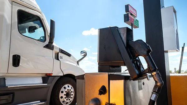 A white tractor is shown next to a diesel pump and Pilot fuel station sign with prices in the background.
