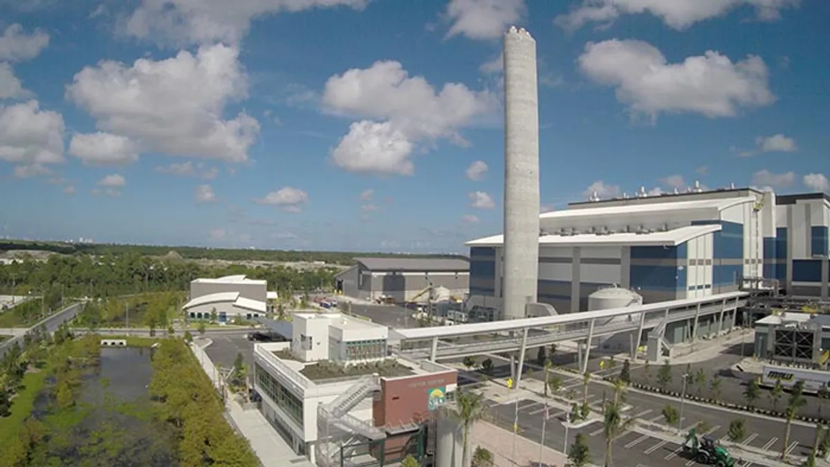 A multi-story production facility with a large, tall smokestack depicted in a picture taken from the air on a sunny day.