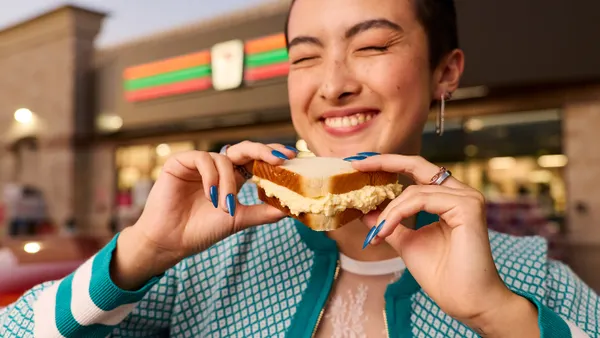 A photo of aperson holding an egg sandwich outside of a store. A Sign above the door on the store says 7-Eleven.