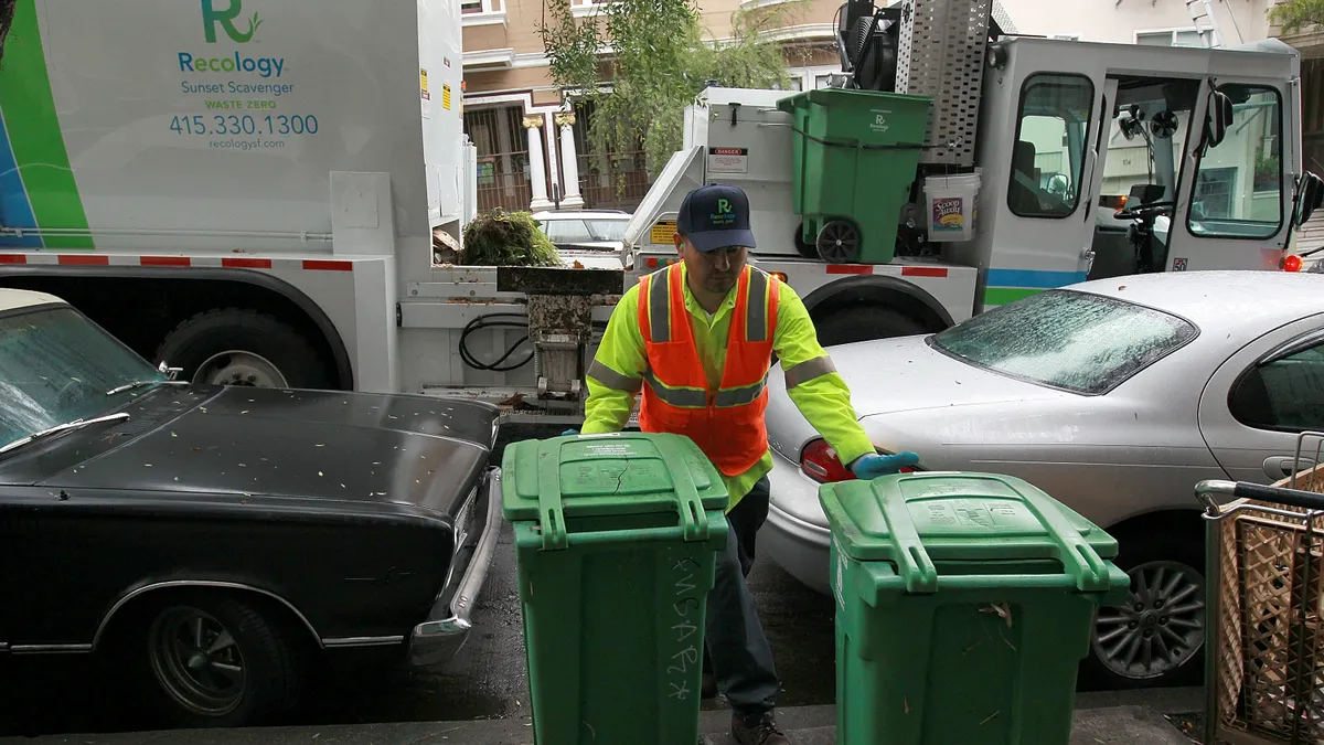 Worker pulling two waste collection carts toward a truck