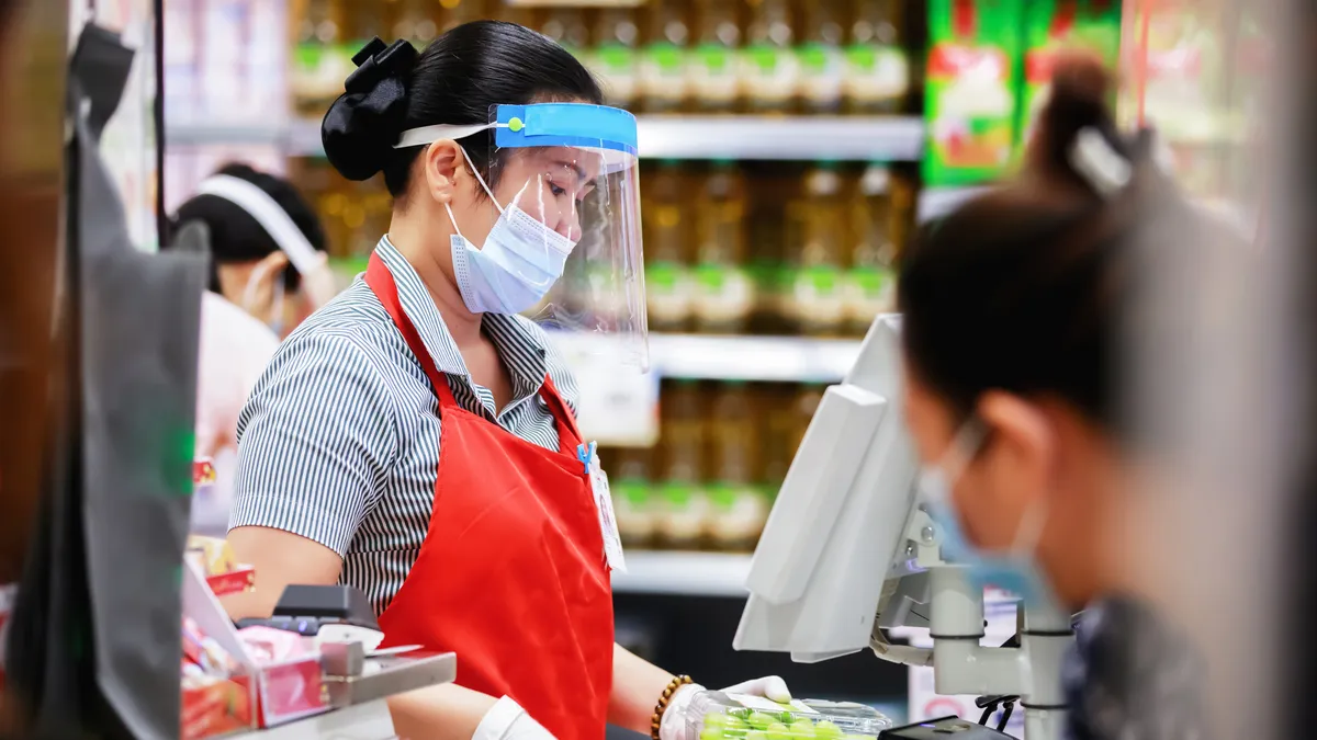 Female supermarket cashier in medical protective mask working at supermarket. covid-19 spreading outbreak