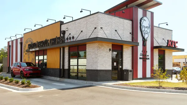 A car drives to a drive-thru window at a Kentucky Fried Chicken storefront.