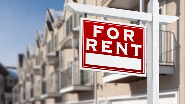 A row of homes with a red sign in the foreground that reads "FOR RENT."