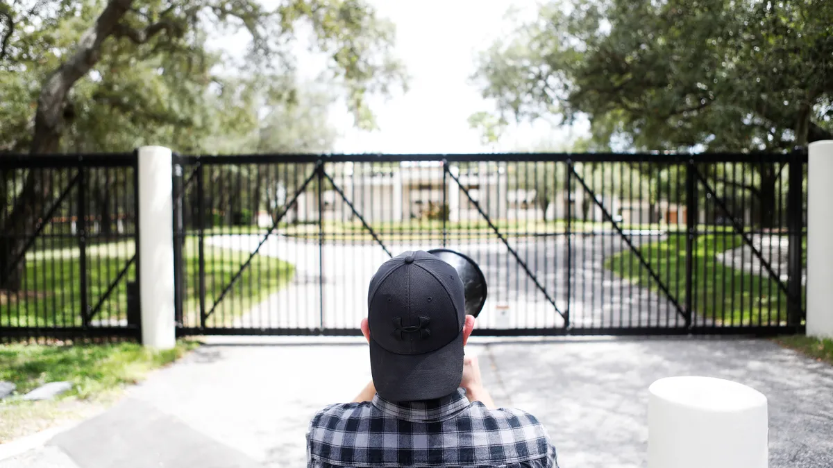 A person wearing a hat stands with a bullhorn in front of a fence.