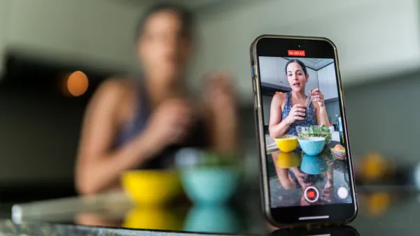 Close-up of a mobile phone recording a young woman vlog preparing salad in kitchen at home