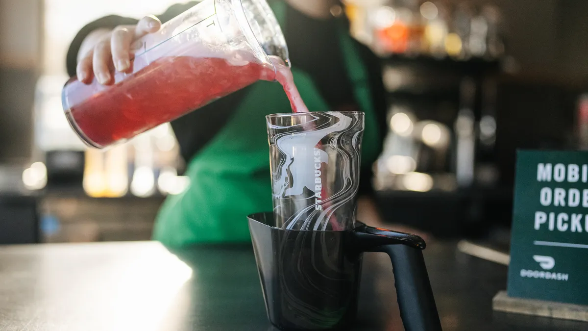 A Starbucks worker pours a beverage into a cup meant to represent a customer's personal drinkware.