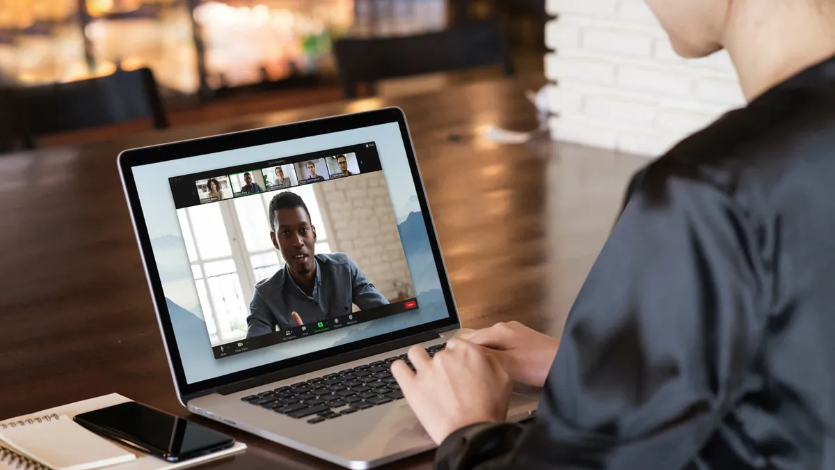 A person sitting at a desk while connected to a videoconference from a laptop