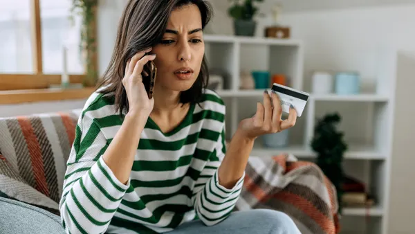 A concerned woman is on the phone and holds a credit card in her other hand.
