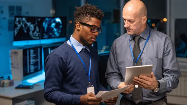 Two elegant intercultural businessmen discussing data in digital tablet held by mature programmer or it-engineer