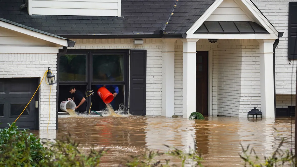 People use buckets to throw floodwater out the windows of a house surrounded by flooding.