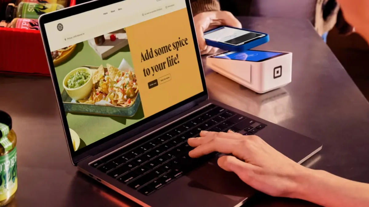 A laptop with a picture of a nachos and guacamole dish is right next to a Square mobile device processing a smartphone. A hand reaches out to the laptop.