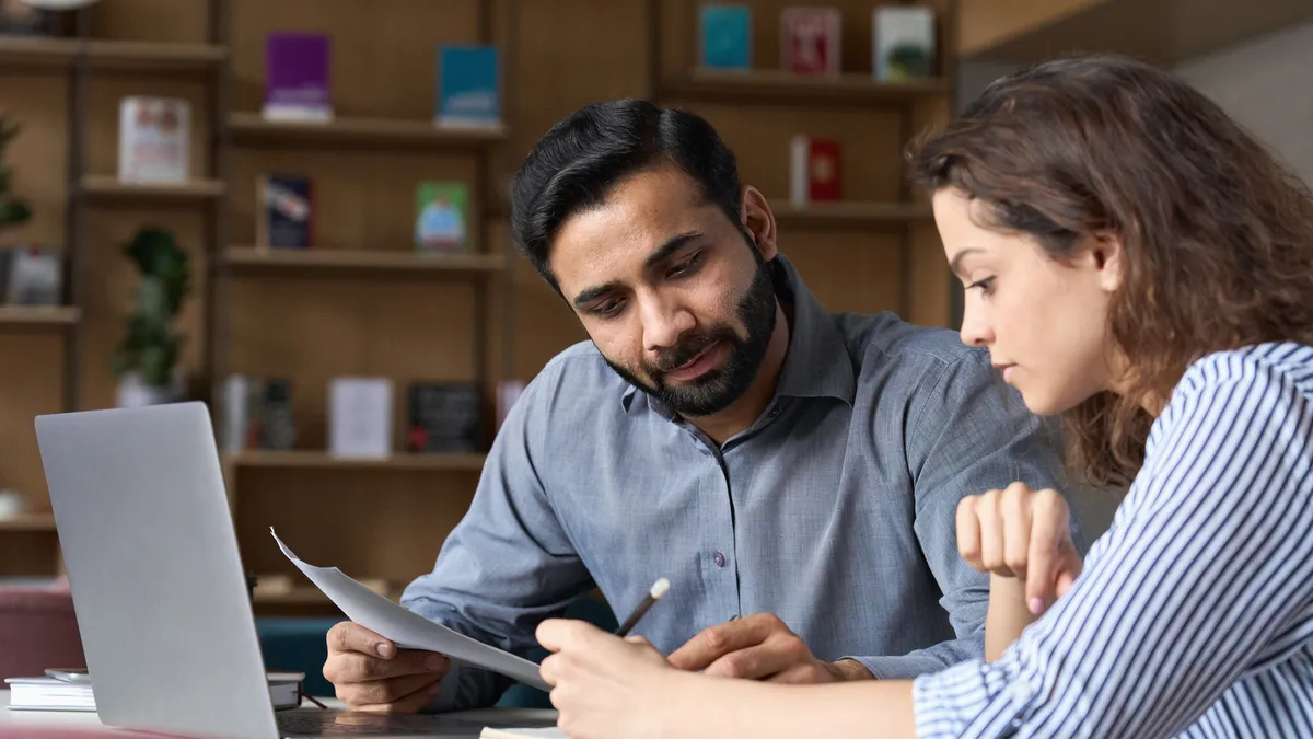 Two people work together in an office looking at papers.