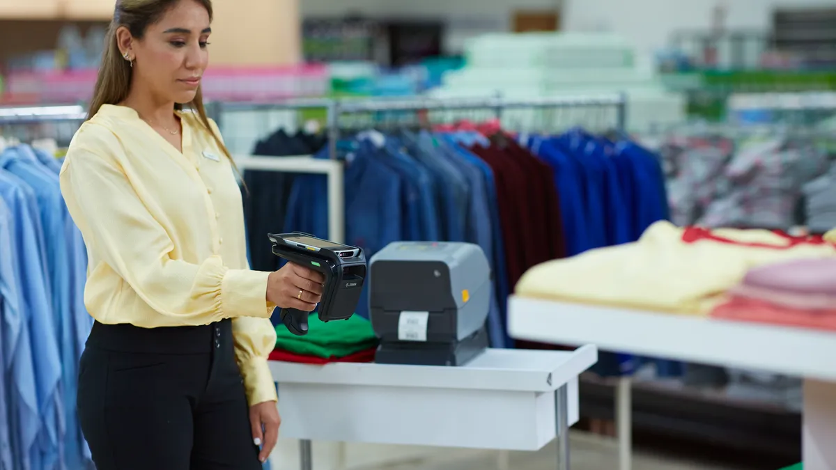 An employee in a story holding a sku reader surrounded by clothes