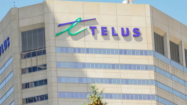 A closeup photo shows the top floors of an office building that bears the name "TELUS" in purple alongside the company's green-and-purple logo