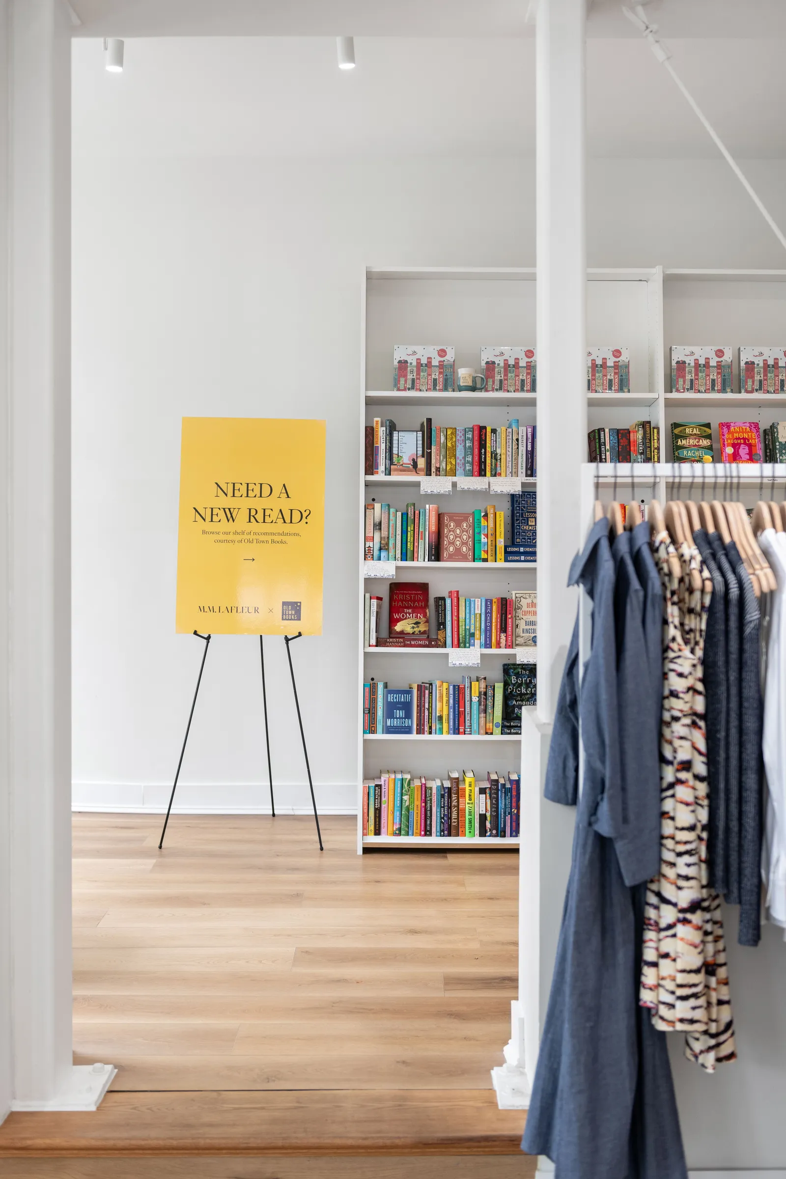 A bookshelf stands in the background of a clothing store, with a rack in the foreground displaying workwear.