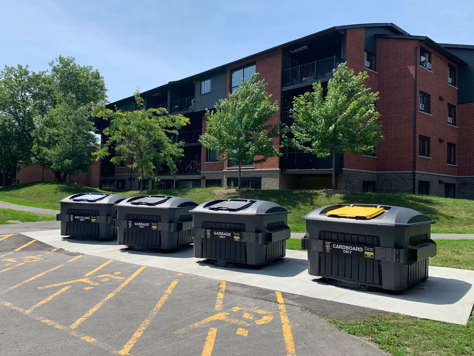 A row of four waste bins in front of an apartment building.