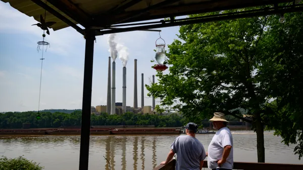Two people look across a river at smoke stacks with white steam coming out of them.