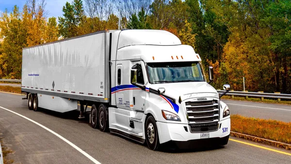 A white TFI International tractor-trailer drives on a road.