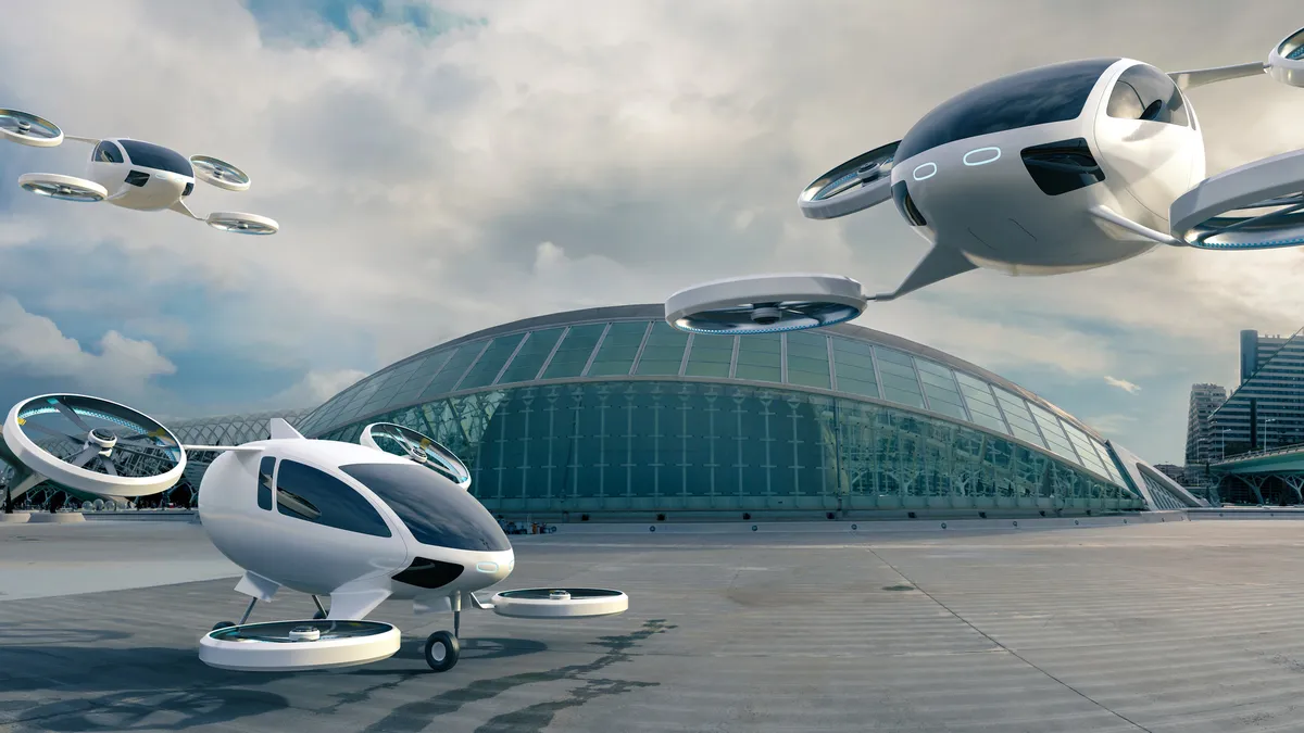 A fleet of white eVTOL aircraft with four rotors, one parked with landing gear on concrete surface in front of glass terminal building and others in midflight.