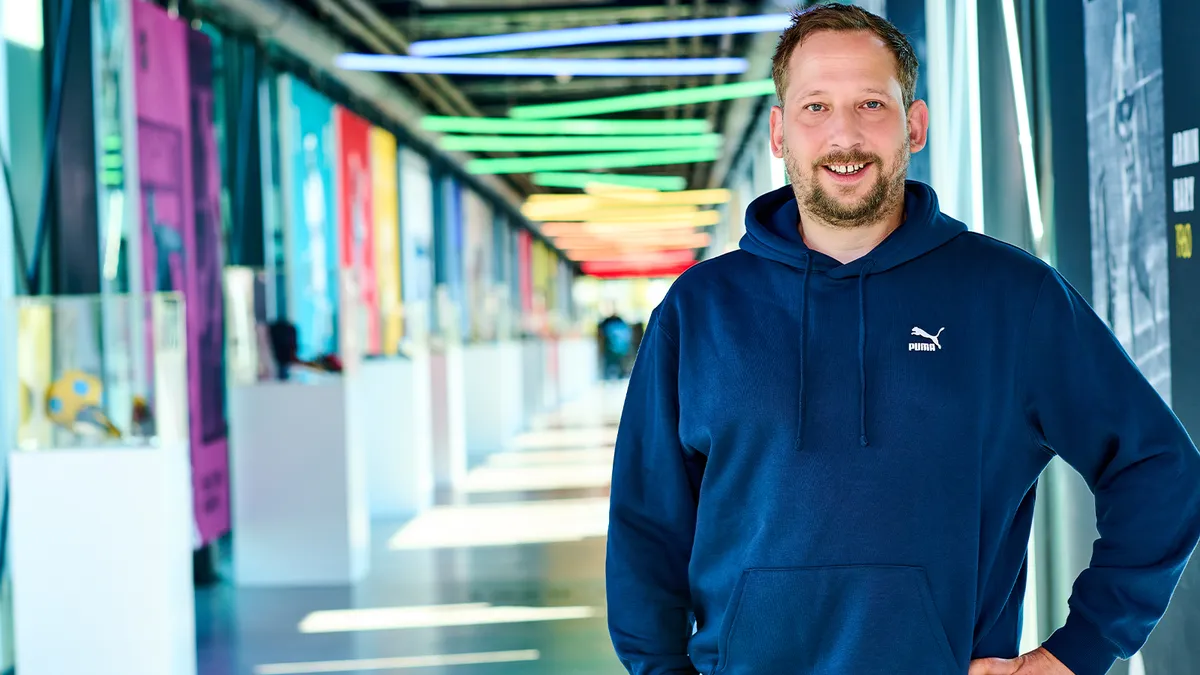 A headshot of Erik Janshen in a colorful hallway with a blue Puma sweatshirt on.