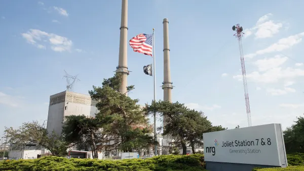 A power plant seen against a blue sky with an American flag in front and a sign that says "Joliet Station 7&8 Generating Station"