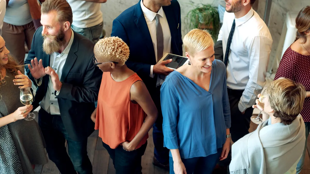 A wide view of coworkers at a party talking. Some are holding alcoholic beverages.